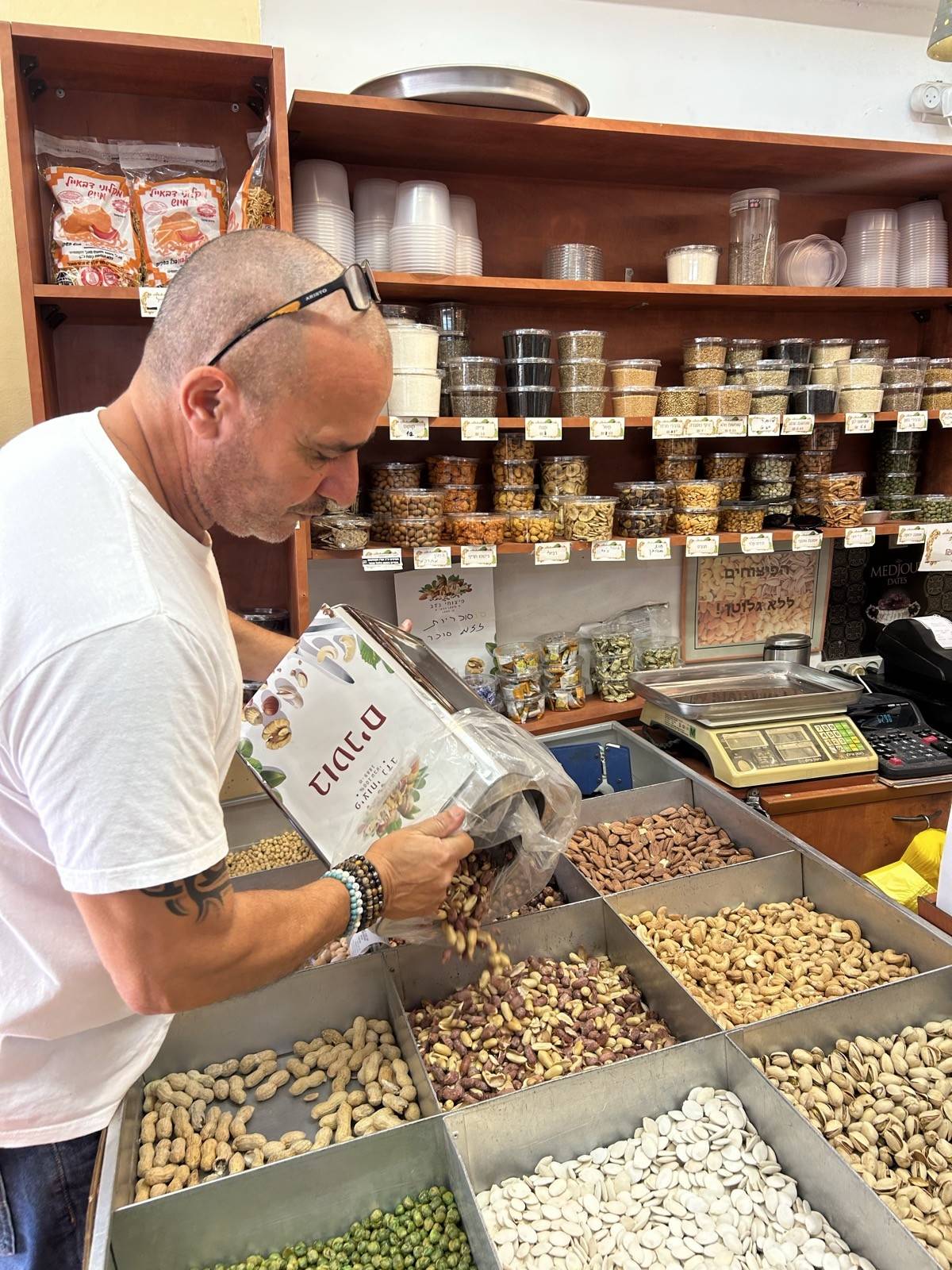 יוסי נדב יוצק אגוזים טריים לתיבות הפיצוחים בחנות באלקנה